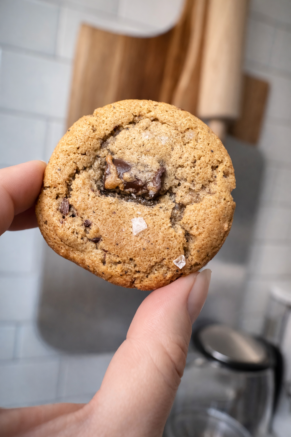 Hand holding a chocolate chip cookie in a kitchen setting