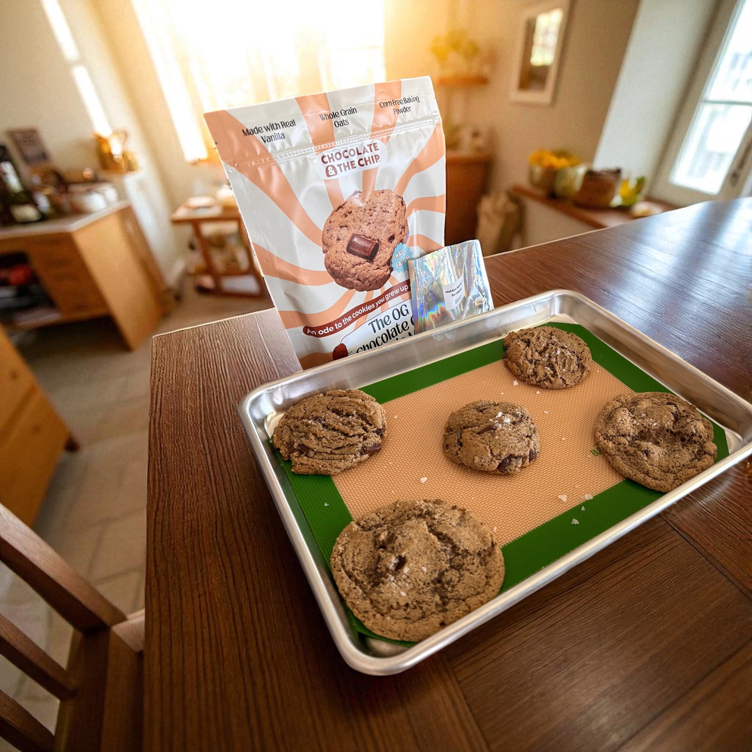 Baked cookies on a baking tray with a package of cookie mix in a kitchen setting.
